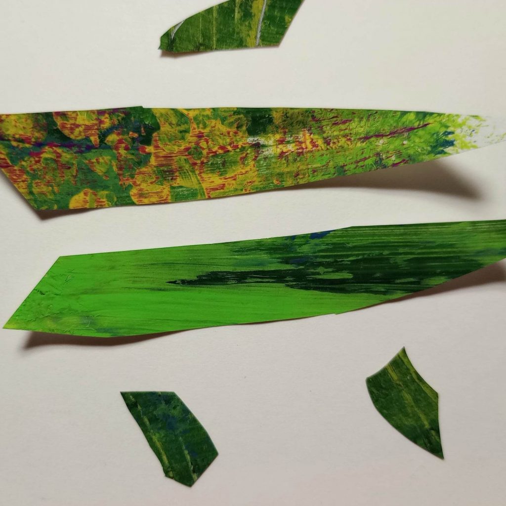 Bottom fin pieces of cut paper fish in Eric Carle style. Green with stripes. Body pieces and most of upper fin showing, too.